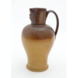 A Doulton Lambeth two tone stoneware jug with relief mask detail to neck. Impressed marks under.