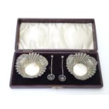 A cased pair of silver salts with embossed decoration and salt spoons with shell formed bowls.