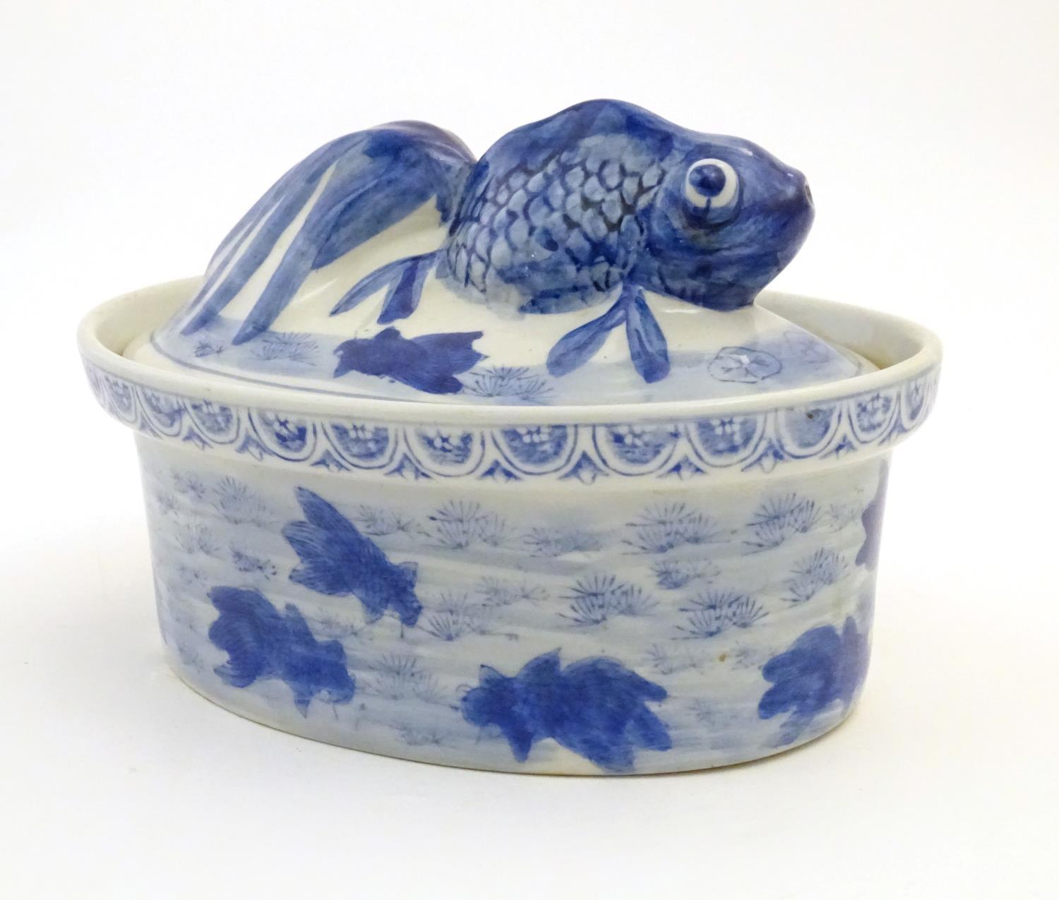 A Chinese blue and white dish and cover of oval form, the lid surmounted by a fish in relief, the