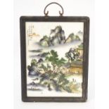 A Chinese ceramic panel depicting figures, boats and buildings amongst a mountainous landscape,