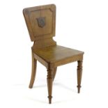 A late 19thC oak hall chair with a tapering back rest, armorial to the centre and raised on tapering