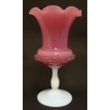 A glass vase, the pink glass body with wavy rim and clear frilled decoration, raised over a milk