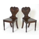 A pair of Regency oak hall chairs with carved and scrolled backrests containing shields to the