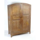 An early 20thC limed oak wardrobe in the manner of Heals with a bowed and carved top above two