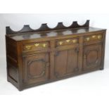 An 18thC oak dresser base with a shaped upstand above three short drawers with brass back plates