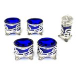 An Art Nouveau silver cruet set comprising four salts and a pepper with blue glass liners and scroll