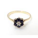 A 9ct gold ring set with central diamond bordered by 6 sapphires in a cluster setting. Ring size