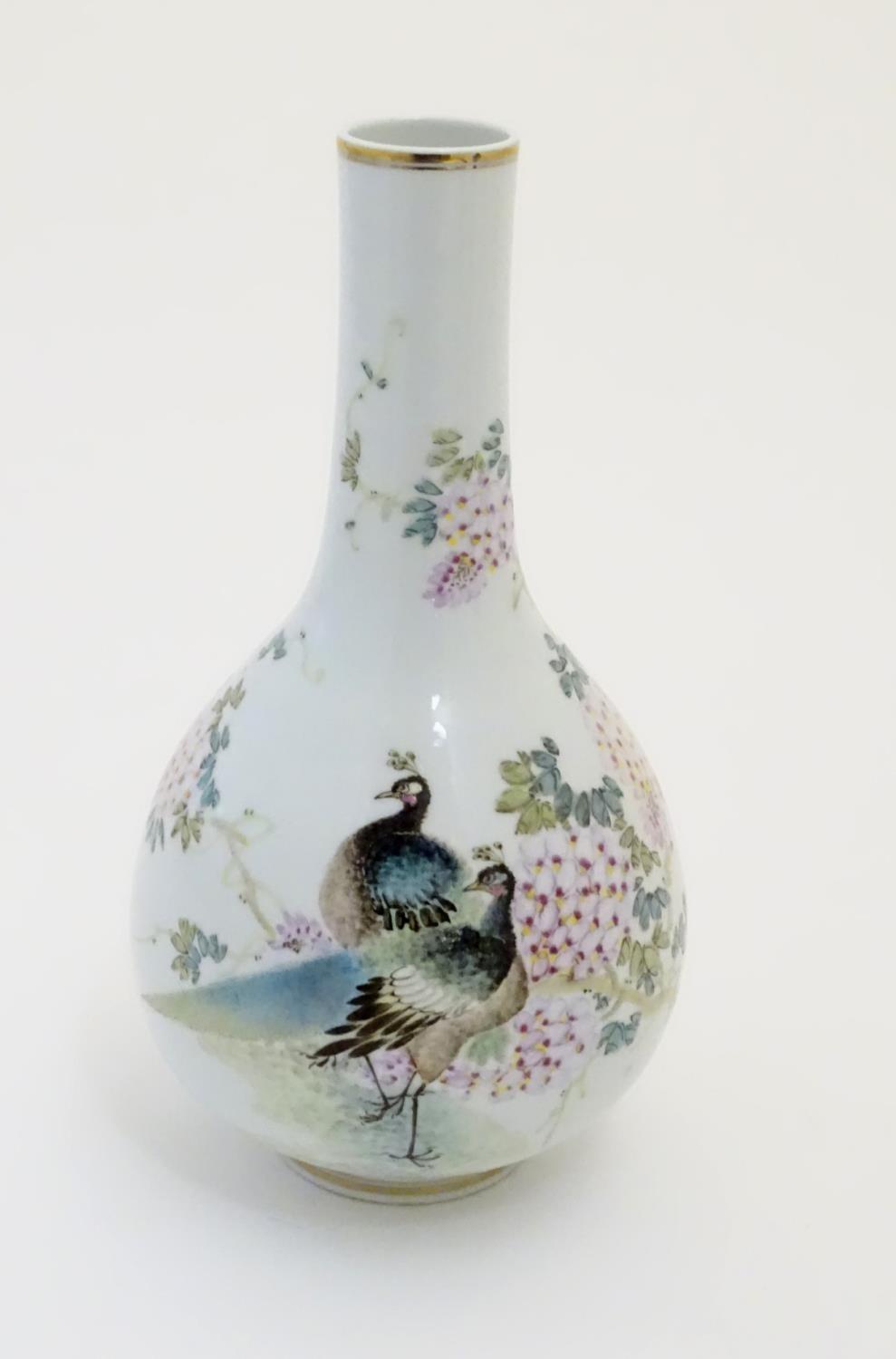 A Chinese globular vase with an elongated neck decorated with peacocks and flowers in a landscape,