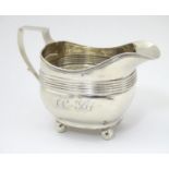 A George III silver cream / milk jug with banded decoration raised on four spherical feet.