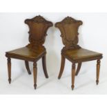 A pair of Victorian oak hall chairs with shaped and carved backrests above gadrooned front rails and