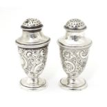A pair of silver pepper pots with embossed formal and C-scroll decoration, hallmarked Sheffield 1897