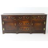 An 18thC oak dresser base with five short drawers having swan neck handles and two cupboards to