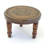 A 20thC carved stool with three turned legs, the top with carved foliate roundel detail and carved