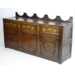 An 18thC oak dresser base with a shaped upstand above three short drawers with brass back plates and