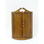 A late 18thC bowfronted oak corner cupboard with a swans neck pediment above mahogany crossbanded