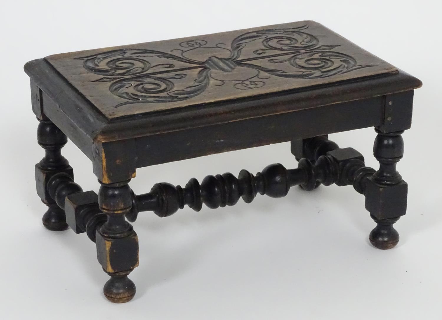 An early 20thC footstool with a carved top above four turned legs united by a H-stretcher. 13"