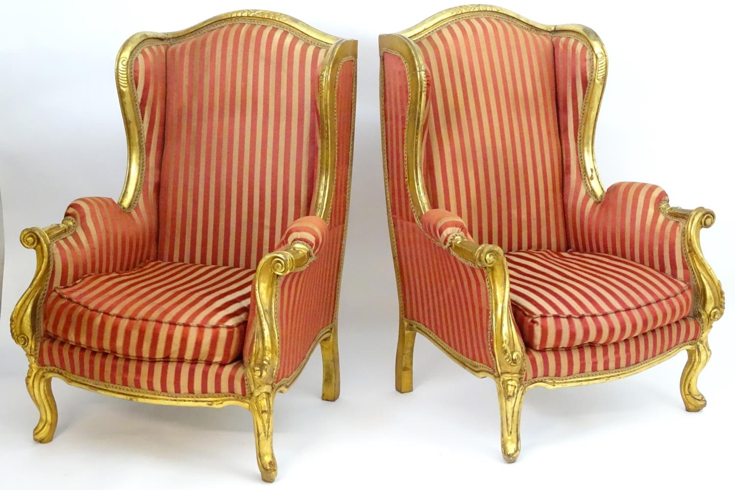 A pair of mid 20thC large gilt wingback armchairs, having moulded frames with floral decoration,