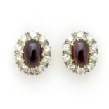 A pair of bespoke gold stud earrings set with central garnet cabochon bordered by 10 diamonds. The