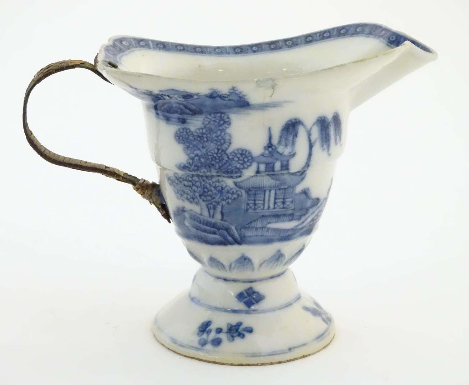 A helmet jug with blue and white decoration with a stylised landscape scene with pagodas,