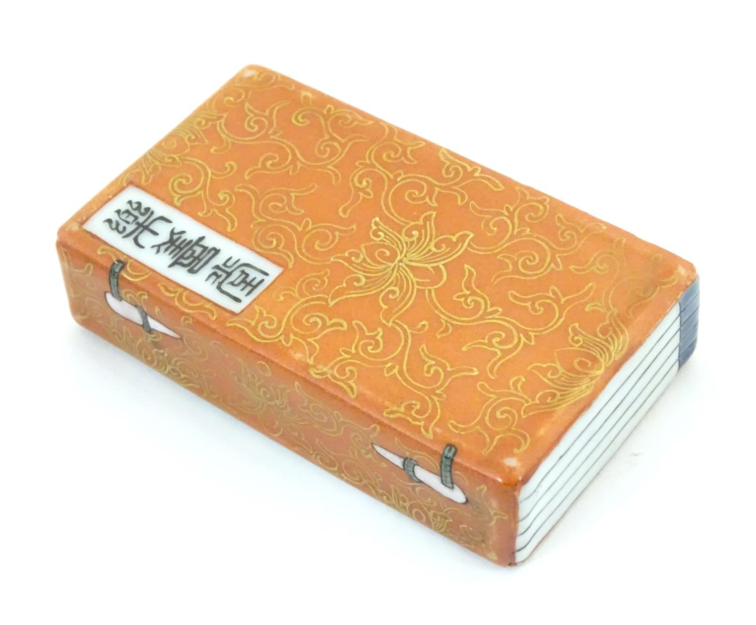 A Chinese porcelain model of a book with scrolling gilt foliate detail and character marks.