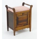 An Edwardian piano stool with an upholstered top above two handles and having a panelled fall front.