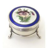A silver pill box with Suffragette pansy enamel decoration to lid hinging open to reveal a gilded