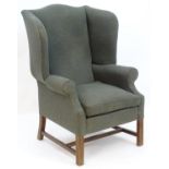 A 20thC wingback armchair with a shaped top, scrolled arms and standing on chamfered legs united