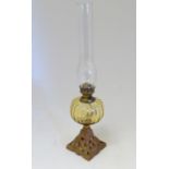An early 20thC oil lamp, the yellow-gold glass reservoir supported by a gilt cast metal base with