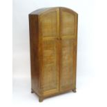 An early 20thC limed oak oak Heals wardrobe with a domed top above two panelled doors with turned