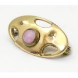 An Arts & Crafts gilt metal brooch set with pink stone cabochon. Marked to reverse with monogram for