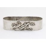A sterling silver napkin ring of ovoid form with hammered detail and stylised crocodile