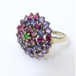 A 9ct gold ring set with a profusion of stones, the central emerald surrounded by amethyst, red