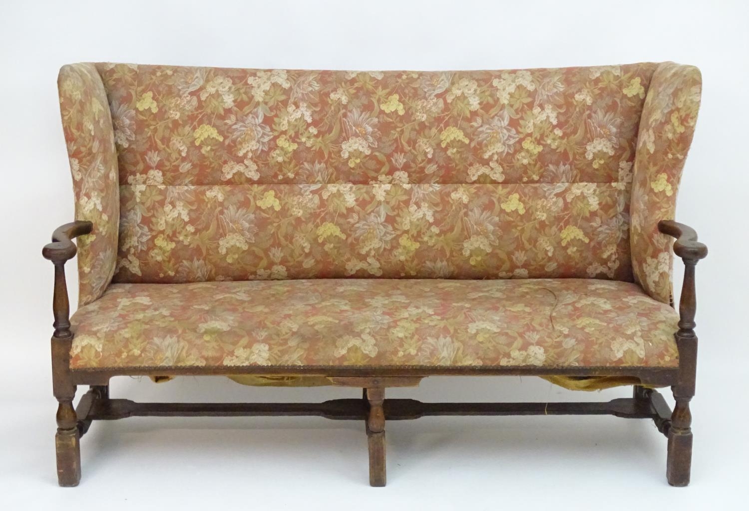 A mid 18thC wingback sofa with scrolled arms and an upholstered backrest and seat above a
