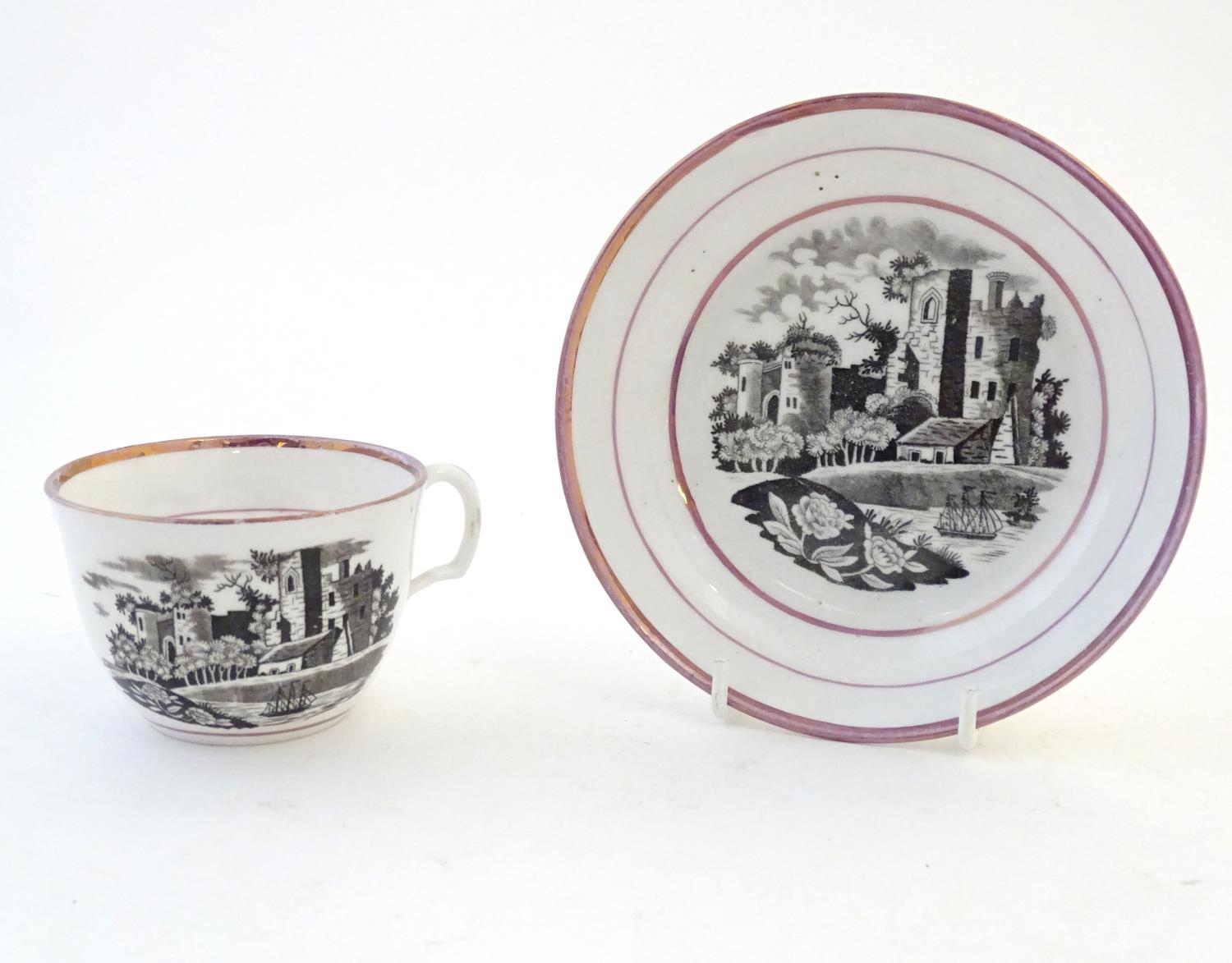 A tea cup and saucer with monochrome transfer decoration depicting a river landscape with a ship and