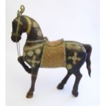 A 20thC carved hardwood standing horse with one leg raised, a copper saddle and brass reigns and