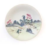 A Chinese plate decorated with a landscape scene with a boat on a river. With red foliate motifs