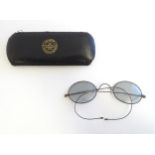 A cased pair of early 20thC spectacles / glasses with a steel frame, tinted oval lenses and flexible