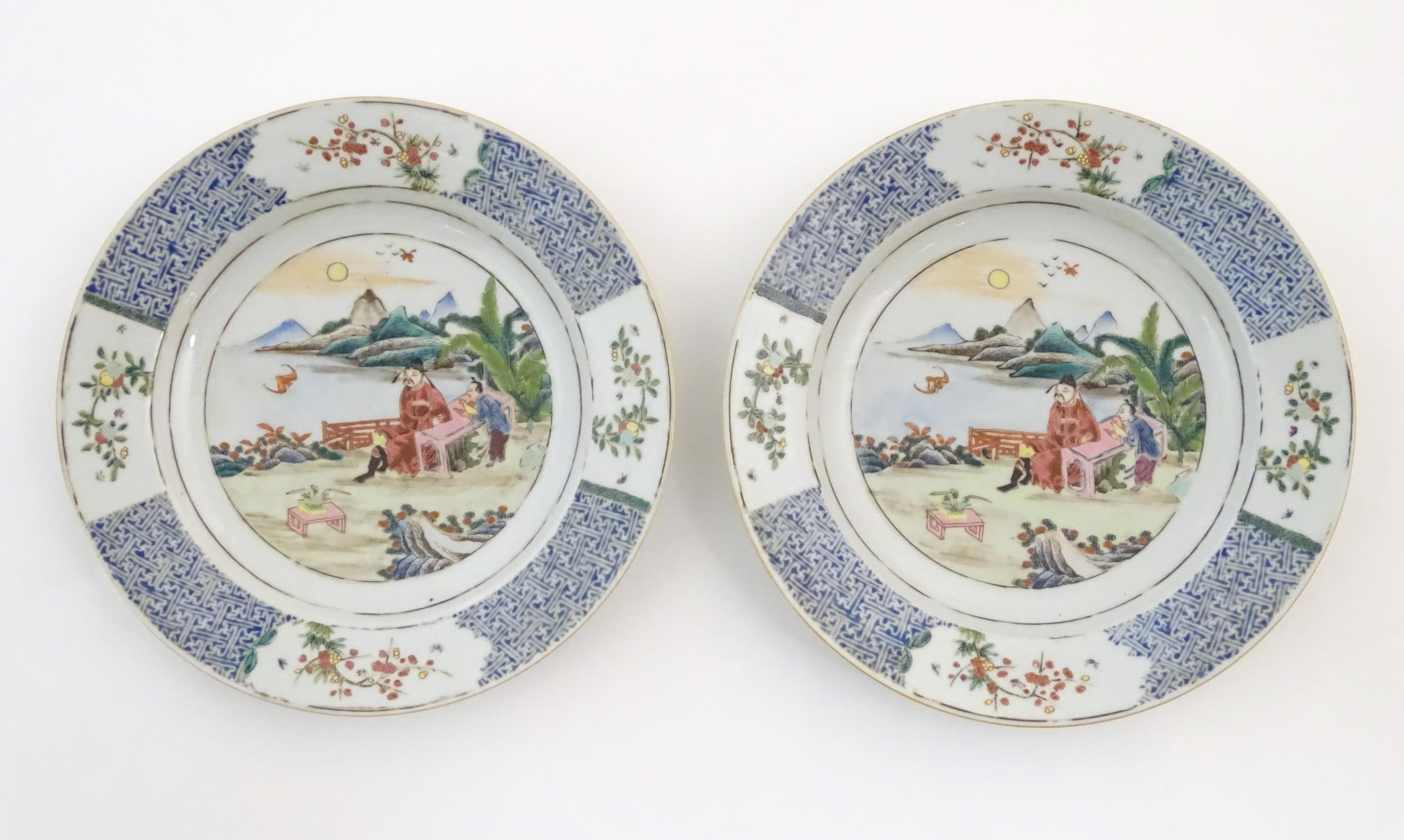 A pair of Chinese plates depicting a two figures in a garden watching a bat, with sea and