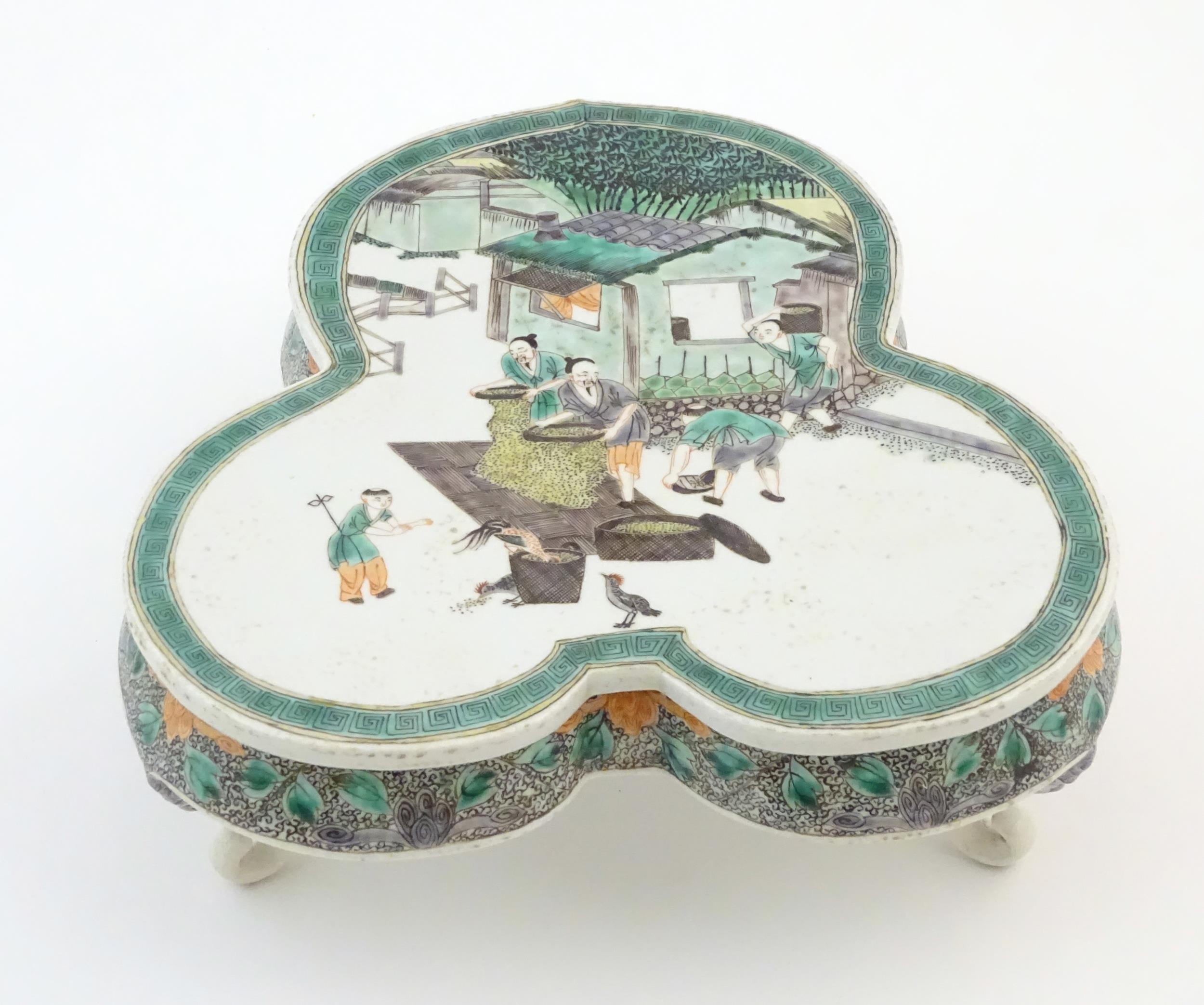 A Chinese famille verte stand of trefoil form depicting figures sifting grain and shooing