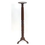 A late 19thC / early 20thC mahogany torchiere with a dished top above a reeded and carved stem