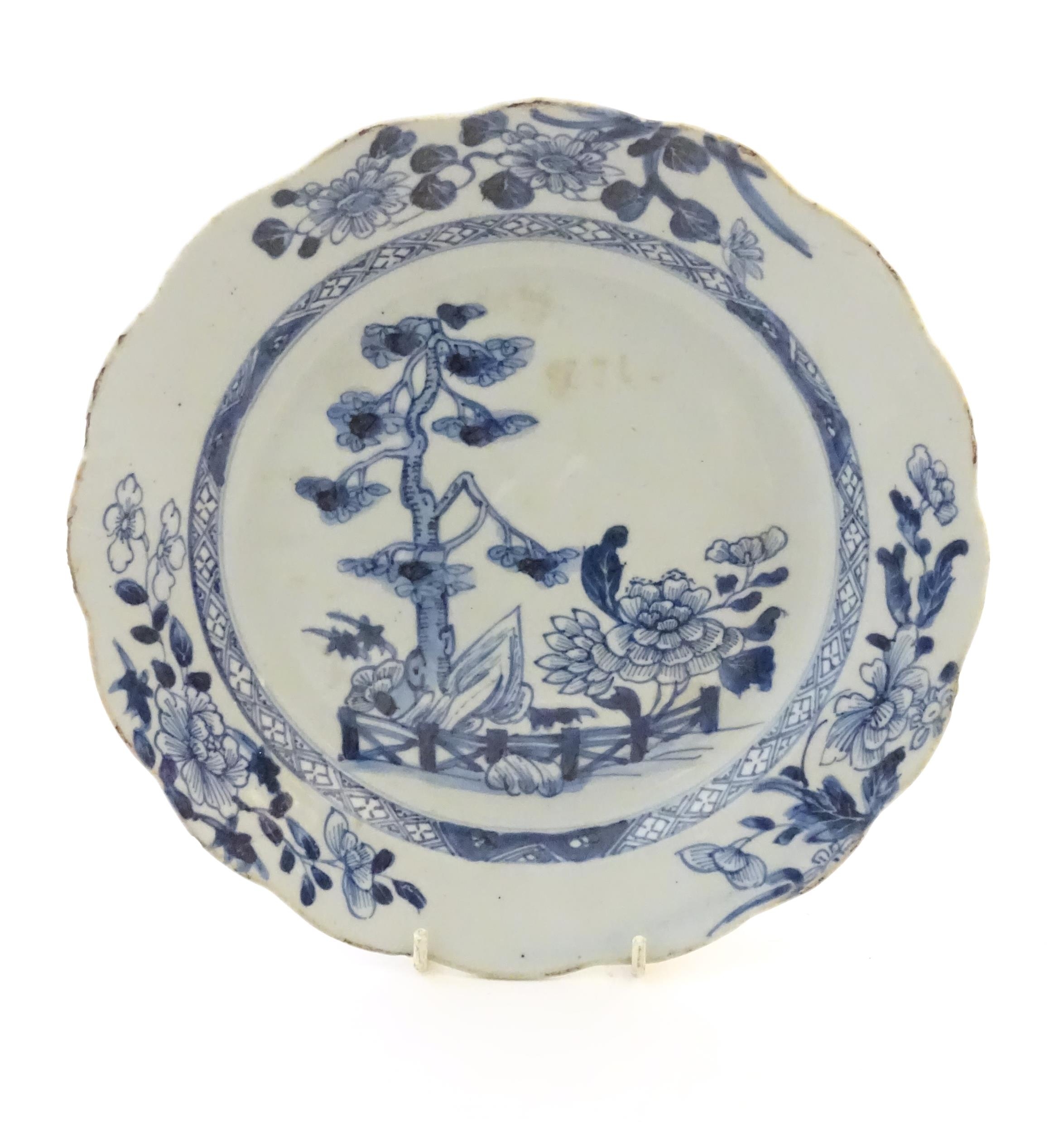 A Chinese blue and white plate with a lobed rim decorated with a landscape scene with trees and