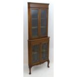 An early 20thC mahogany corner cabinet with a moulded cornice above two glazed doors, the base