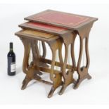 A nest of three mid / late 20thC mahogany tables with inset leather tops and lyre shaped supports.