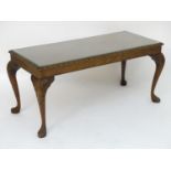 A mid 20thC walnut coffee table with a carved surround and raised on four legs with acanthus
