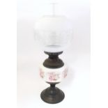 An early 20thC table oil lamp, the brass column with ceramic mid section decorated with roses and