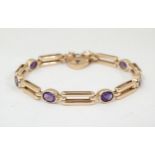 A 9ct gold bracelet of link form set with oval amethysts. With safety chain and padlock formed clasp