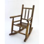 An early 20thC child's rocking chair with spindle turned back rest and turned wooden arms. 22" high.
