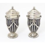 A pair of silver pepperettes of urn shape with bow and swag detail and blue glass liners. Hallmarked