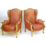 A pair of mid 20thC large gilt wingback armchairs, having moulded frames with floral decoration,