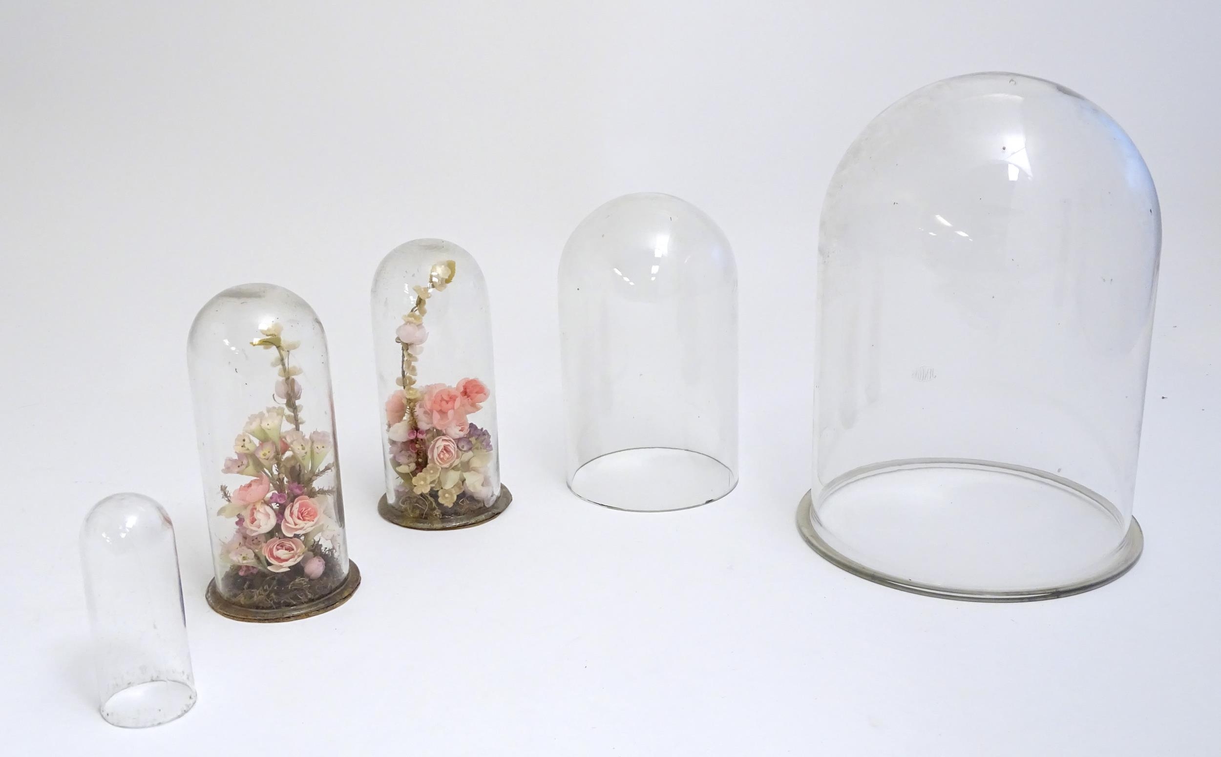 Five glass domes, to include a pair containing floral displays of artificial flowers. The largest